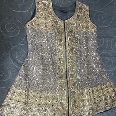 Mysore With Intricate Gold Embroidery (Shirt And Dupatta) - Brand New- Never Worn (Will Go Perfectly With Gold Gharrara Or Cigarette Pants) Material: Shirt & Dupatta: Maysoori/Organza Color: Lilac-Grey With Gold Embroidery And Navy Blue Edge In The Inside Bottom Of Shirt; And At Dupatta Ends (Pulloo). Embroidery: Intricate Gold Tilla, Zari With Navy Blue Beads (See Pics) Sleeves: Included With Half Lining- 19 Inch Length Shirt Style: Flared - No Side Slits. Shirt Length: 33 Inch Approx. Blue Chanderi Embroidered Fabric For Party, Blue Chinon Kurta With Intricate Embroidery, Anarkali Top With Mirror Work For Eid, Blue Embellished Salwar Kameez For Navratri, Embroidered Sleeveless Salwar Kameez For Festive Occasions, Festive Sleeveless Embroidered Salwar Kameez, Festive Embroidered Sleeveless Salwar Kameez, Traditional Sleeveless Salwar Kameez With Intricate Embroidery, Blue Embroidered Chinon Blouse Piece