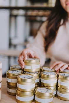 a woman standing in front of stacks of gold and white jars with labels on them