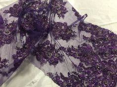 two pieces of purple lace with flowers on them sitting on a white sheeted surface