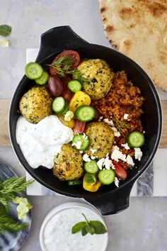 a pan filled with meatballs and vegetables next to pita bread on a table