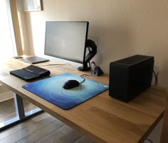 a computer monitor, keyboard and mouse on a wooden desk in front of a window