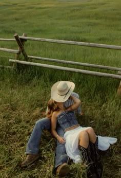 a man and woman laying on the ground in front of a wooden fence with horses behind them