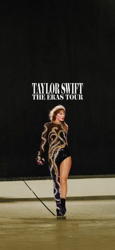 a woman walking down a runway in front of a black wall with the words taylor swift on it