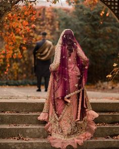 a woman in a pink and gold wedding dress standing on steps with her back to the camera