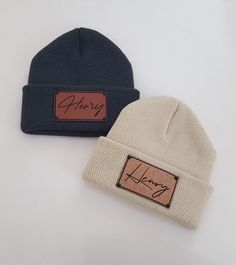 two beanies with leather labels on them sitting next to each other in front of a white background