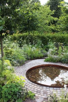 a circular brick patio surrounded by greenery and trees, with a pond in the middle