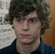 a young man with curly hair looks at the camera while wearing a black shirt and tie