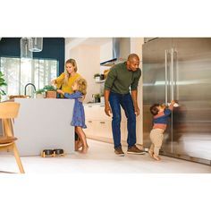 a man, woman and child standing in a kitchen with stainless steel refrigerator freezer