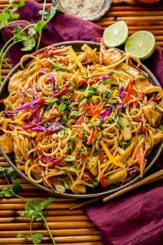 a bowl filled with noodles and vegetables on top of a purple cloth next to limes