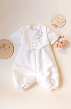 a baby's white outfit and flowers are laying on the floor next to a wooden plaque