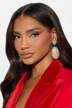 a woman with long dark hair wearing large earrings and a red shirt, looking at the camera