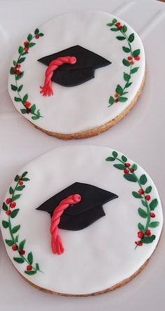 two decorated cookies with graduation caps and holly wreaths are on a white tablecloth