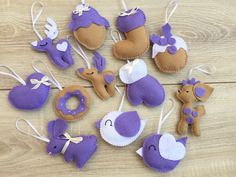 several felt ornaments are arranged on a wooden surface, including purple and white ones with hearts