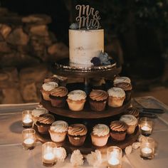 a three tiered cake with cupcakes and candles on the table next to it