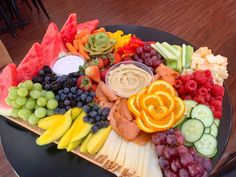 a platter filled with fruits and vegetables on top of a black plate next to a wooden table