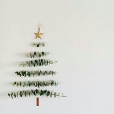 a christmas tree made out of branches and leaves on a white wall with a star hanging from the top