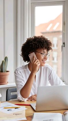 a woman sitting in front of a laptop computer talking on a cell phone