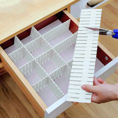 a person is holding scissors in front of a drawer that has several compartments on it