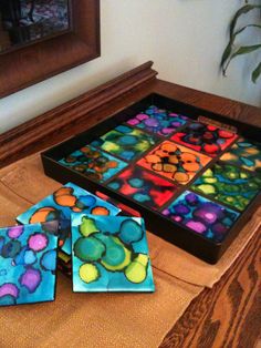 three colorful coasters sitting on top of a wooden table next to a framed painting