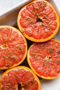 four slices of grapefruit sitting in a white dish on a counter top with herbs