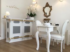 a white dining room table and chairs with gold trim around the edges, in front of a mirror