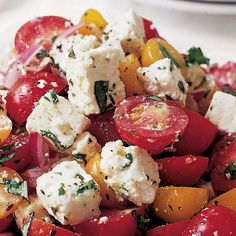 a salad with tomatoes, feta cheese and herbs in it on a white plate