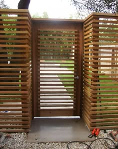 a wooden gate with slats on the sides and an opening in the middle that leads to a grassy area