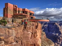 people standing at the edge of a cliff overlooking a building on top of a mountain