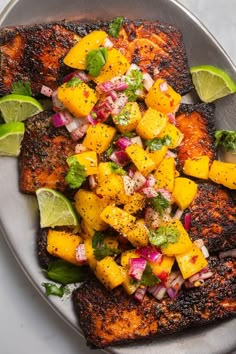 grilled fish with mango salsa and lime wedges on a silver platter, ready to be eaten