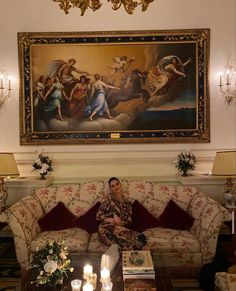 a man sitting on top of a couch in front of a painting above him with candles