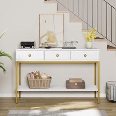 a white and gold console table with two drawers under the stair case next to a potted plant