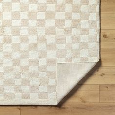 a white rug with squares on it sitting on a wooden floor next to a wall