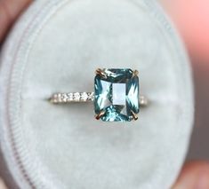 someone is holding a ring with an aqua colored stone in it's middle finger