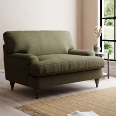 a green couch sitting on top of a wooden floor next to a rug and window