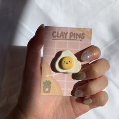 a person holding up a tiny egg in their left hand with the word clay pins on it