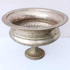 an old silver bowl sitting on top of a white table