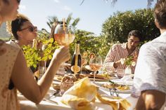 a group of people sitting at a table with wine glasses in their hands and food on the table