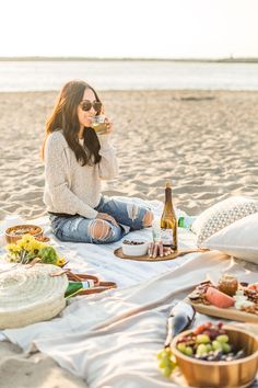 a woman sitting on top of a beach next to food and drinks in front of her