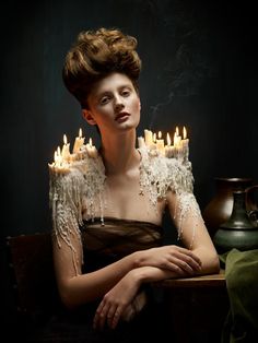 a woman sitting in front of a table with candles on top of her head and arms