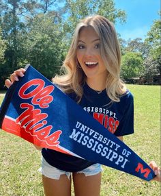 a young woman holding up a mississippi university scarf in the middle of a grassy field