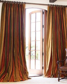 a chair sitting in front of a window with curtains hanging from it's sides