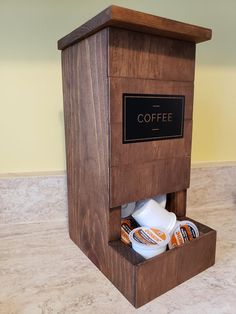 a wooden coffee dispenser with two cups in it and a sign on the side