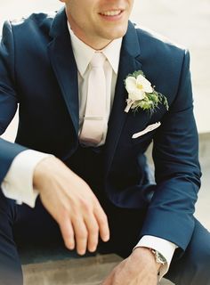 a man in a suit and tie sitting on the ground with his hand on his lapel