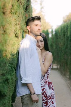 a young man and woman standing next to each other in front of a hedge wall