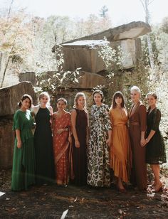 a group of women standing next to each other in front of a stone wall and trees