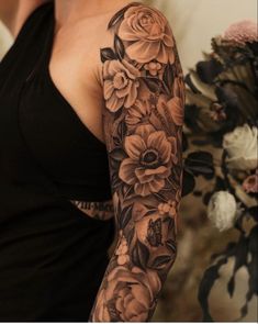 a woman with a black and white flower sleeve tattoo on her left arm is looking at the camera