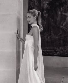 a woman in a wedding dress standing next to a pillar with her hand on the wall