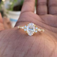 a person's hand holding an engagement ring with three stones on the band and one stone in the middle