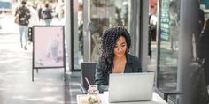 a woman sitting at a table with a laptop in front of her on the street