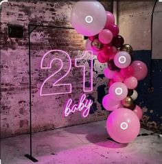 a pink and white balloon arch with the number twenty one baby on it in front of a brick wall